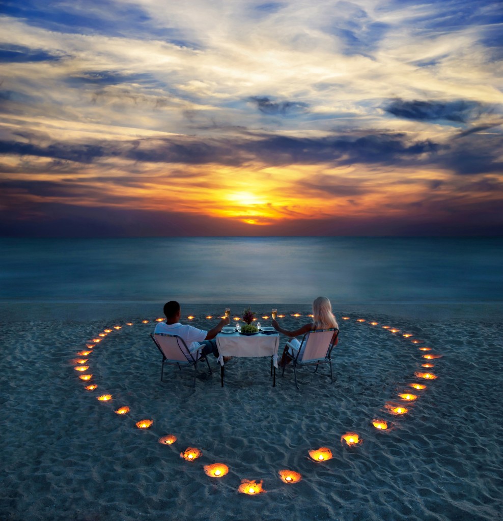 A young couple share a romantic dinner with candles heart on the sea sand beach